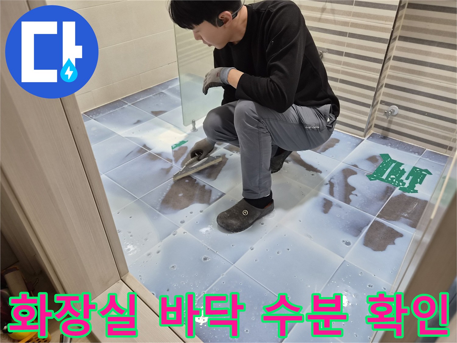 작업자가 화장실 타일 바닥의 젖은 부위를 직접 조사하고 있습니다.