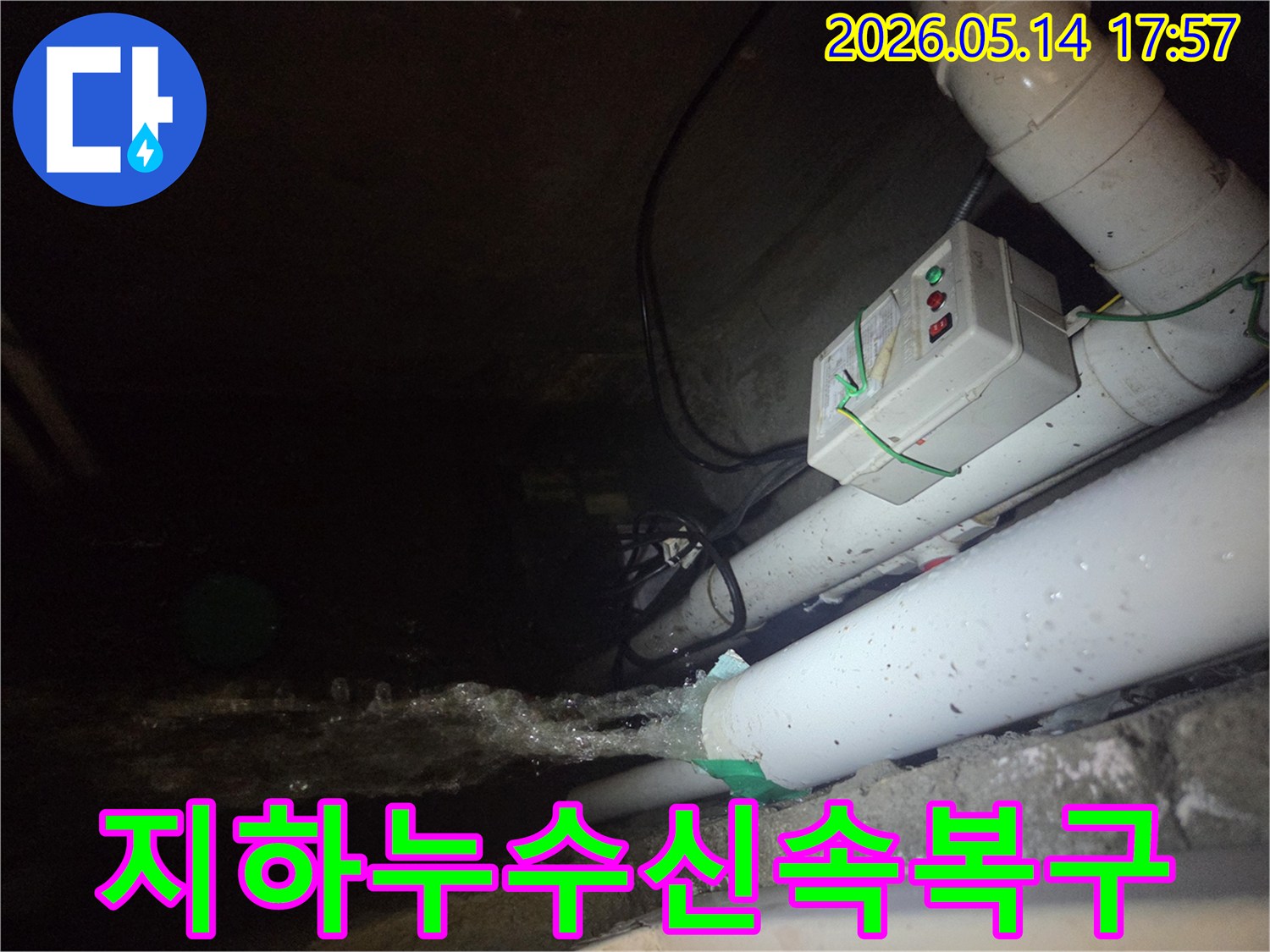 어두운 지하 공간에서-파이프에서 물이 강하게 뿜어져 나오는-주택 지하 누수 현장을 보여주는 사진입니다-전기 제어 박스와 배관들이 함께 보입니다.