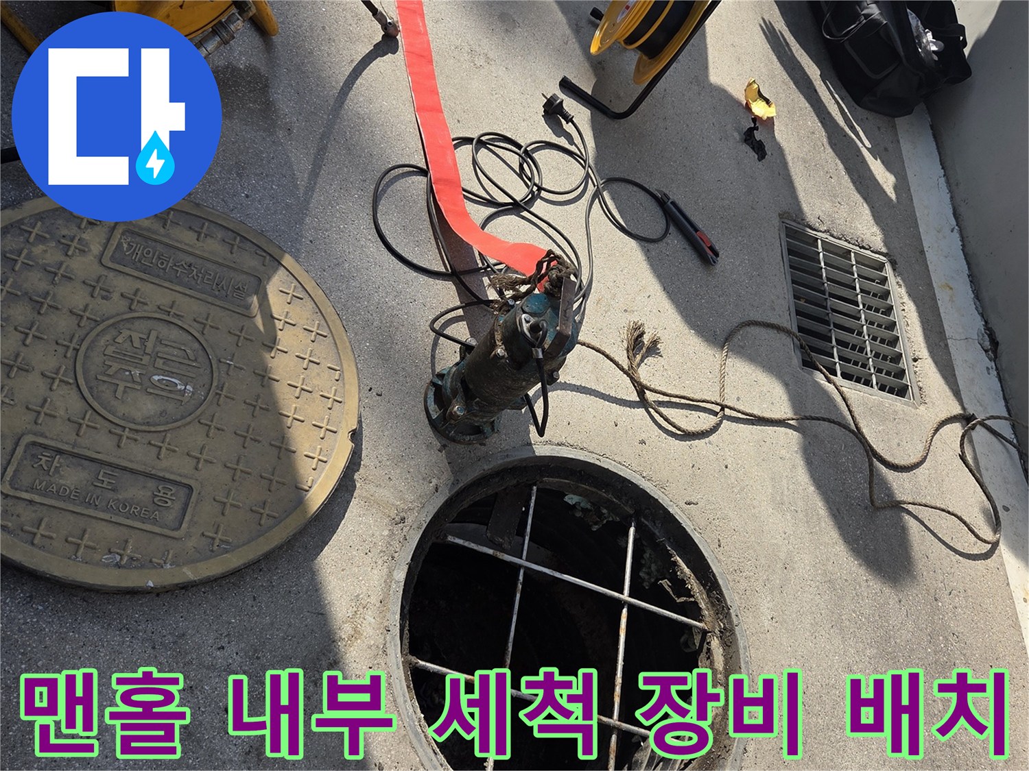 열려 있는 맨홀 입구와 주변에 놓인 고압 세척용 호스 및 릴 장비의 모습입니다.