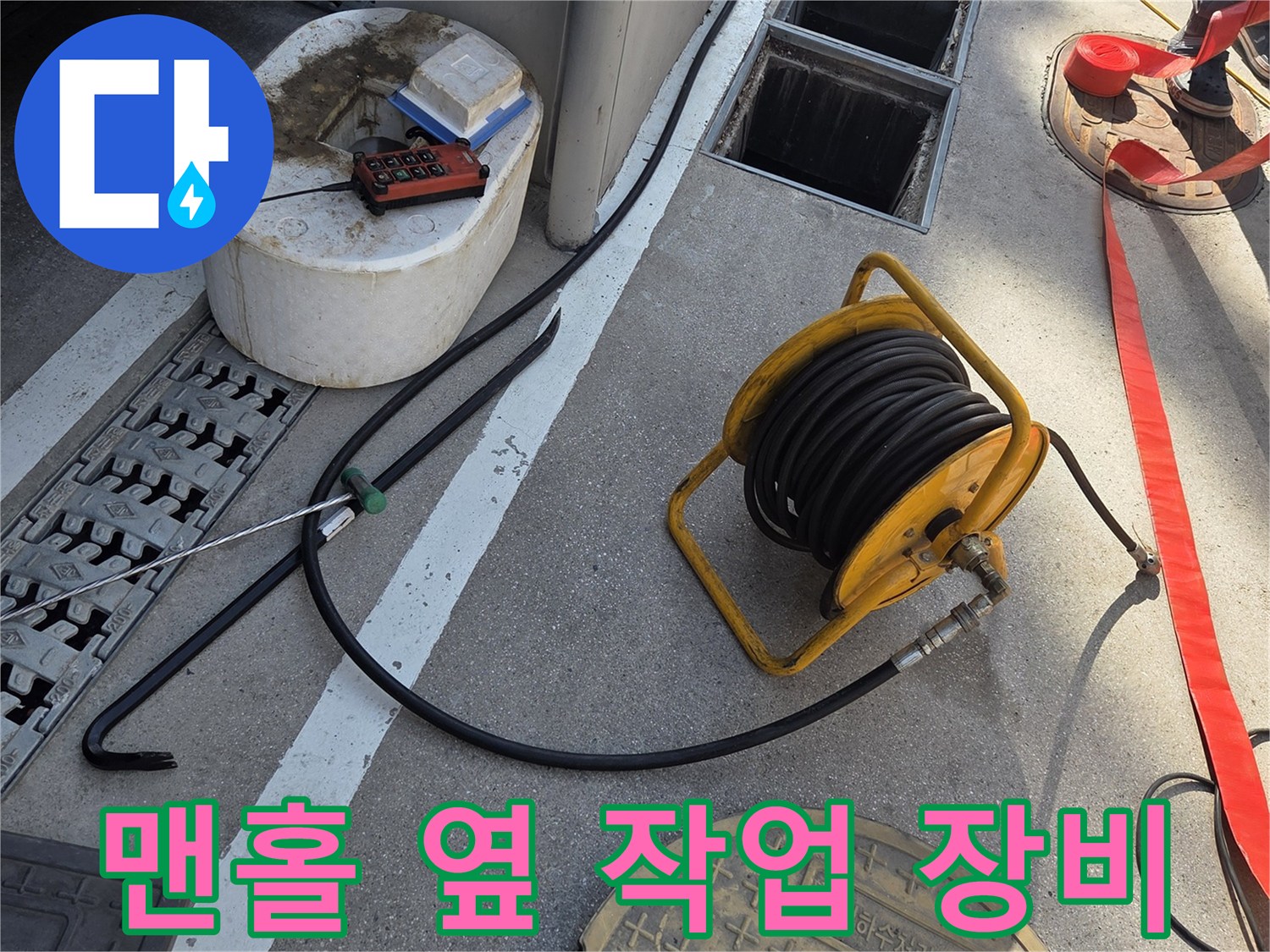 지면의 맨홀 덮개와 세척 작업을 위해 놓인 고압 호스 릴