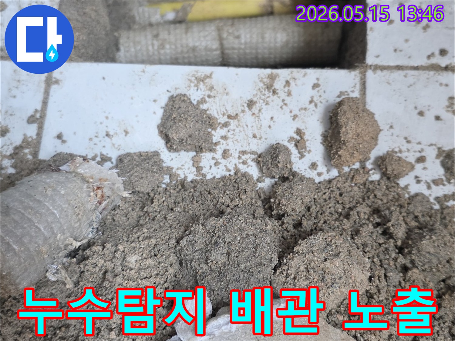 누수 공사 현장에서-바닥을 개방하여-드러난 배관과-주변의 흙더미-그리고-파손된 타일 조각들입니다