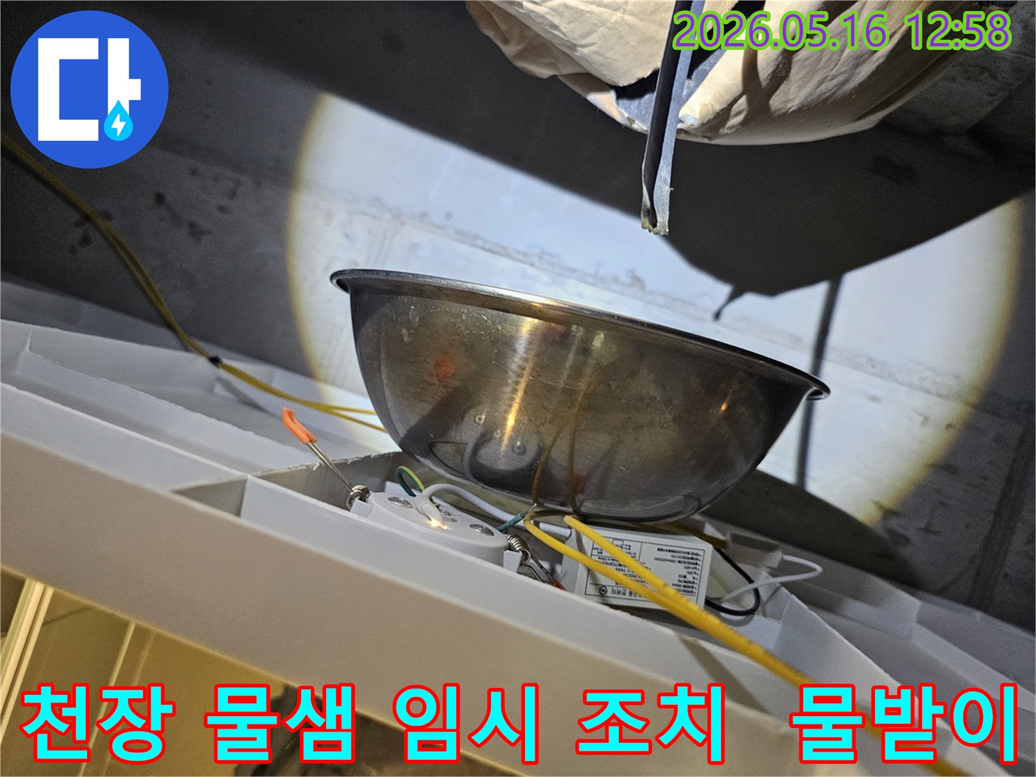 천장에서 물이 새는 것을-스테인리스 그릇으로-받아내며-전기 배선과-조명 장치 주변의-안전 상태를-점검하는 모습