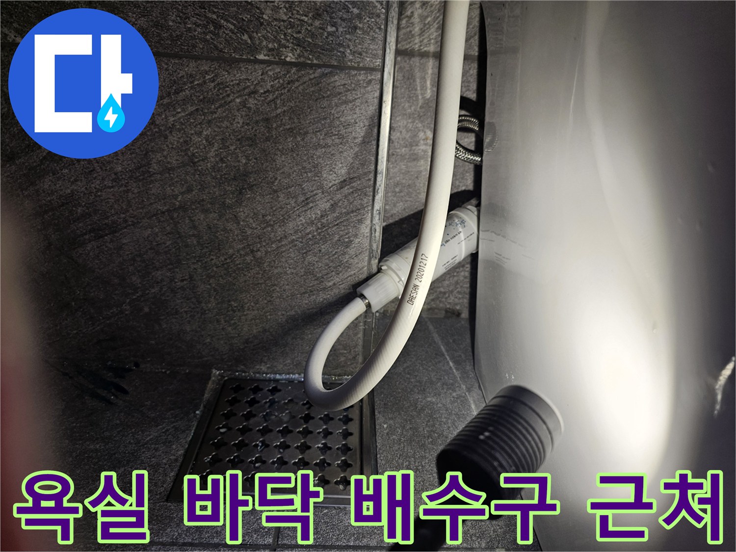 타일 바닥에 설치된 격자 모양의 배수구와 변기 호스 연결부