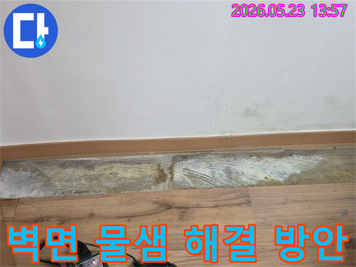 누수 탐지 장비가-바닥에 놓인 채-벽 하단에-발생한-물샘과-습기 흔적을-보여주는-손상된 벽면의-현장 사진