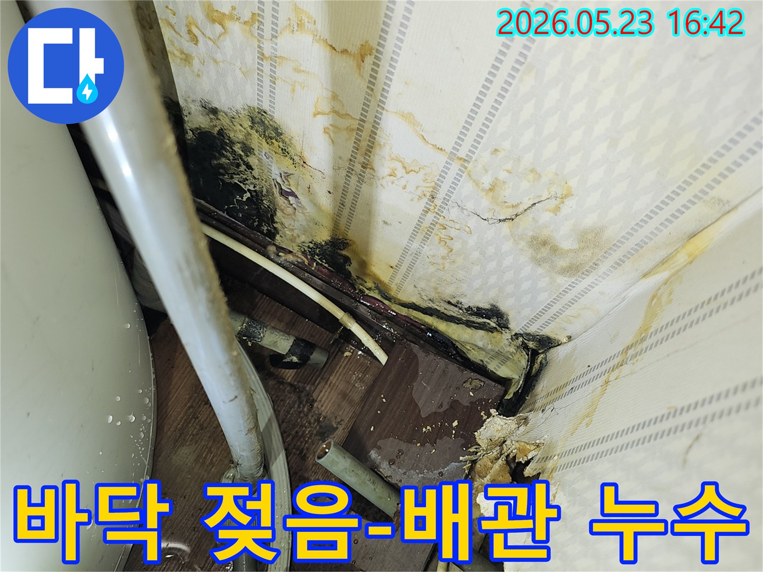 바닥과 벽면이 젖어 있고-노출된 배관 주변에-물이 고여있는-누수 현장 이미지입니다.