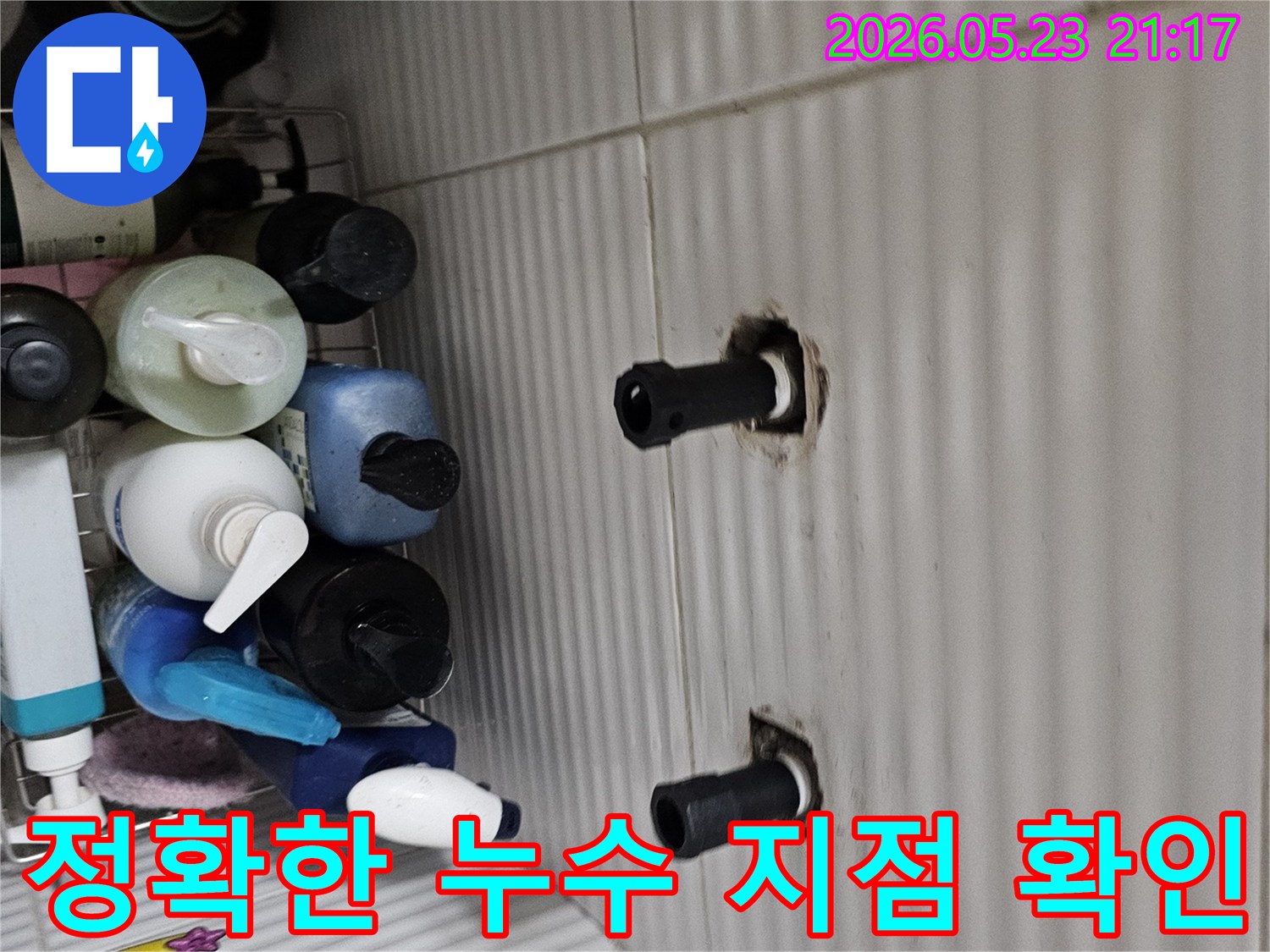 타일 벽면에서 노출된 수도 배관의 연결 부위를-정확한 누수 지점을 찾아내기 위해-면밀히 검사하는 모습입니다.