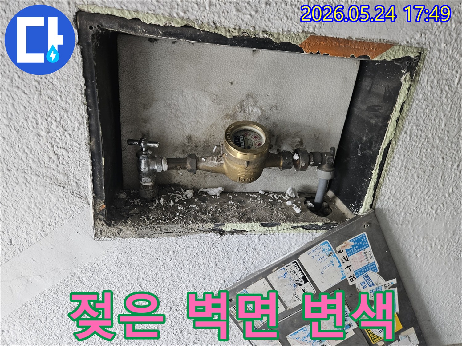 수도 계량기 주변 벽면이 젖어 있고-변색된 흔적이 발견되어-누수를 의심하는 이미지입니다.