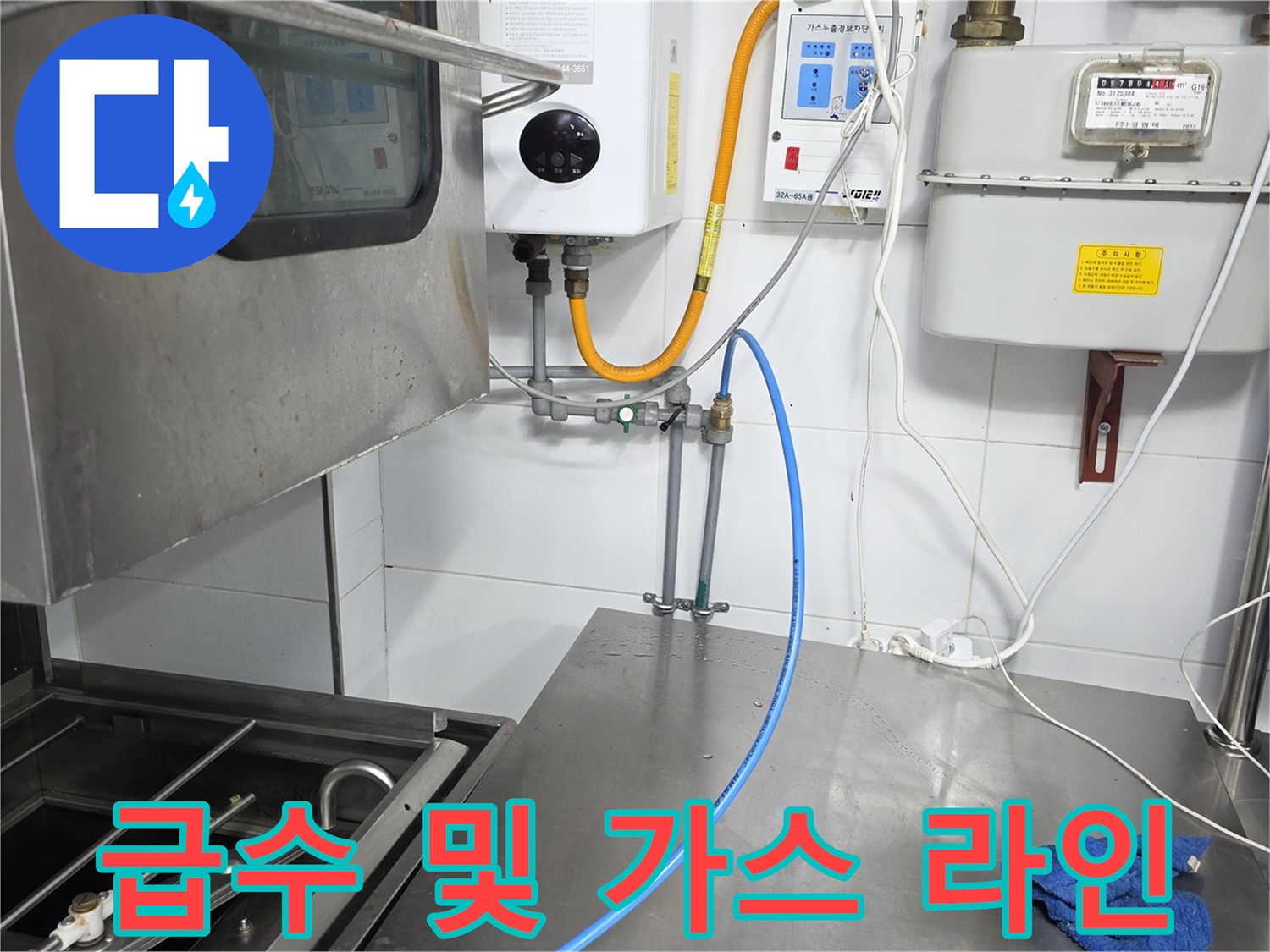 주방 벽면 계량기 부근의 파란색 급수 호스와 노란색 가스 배관 연결부