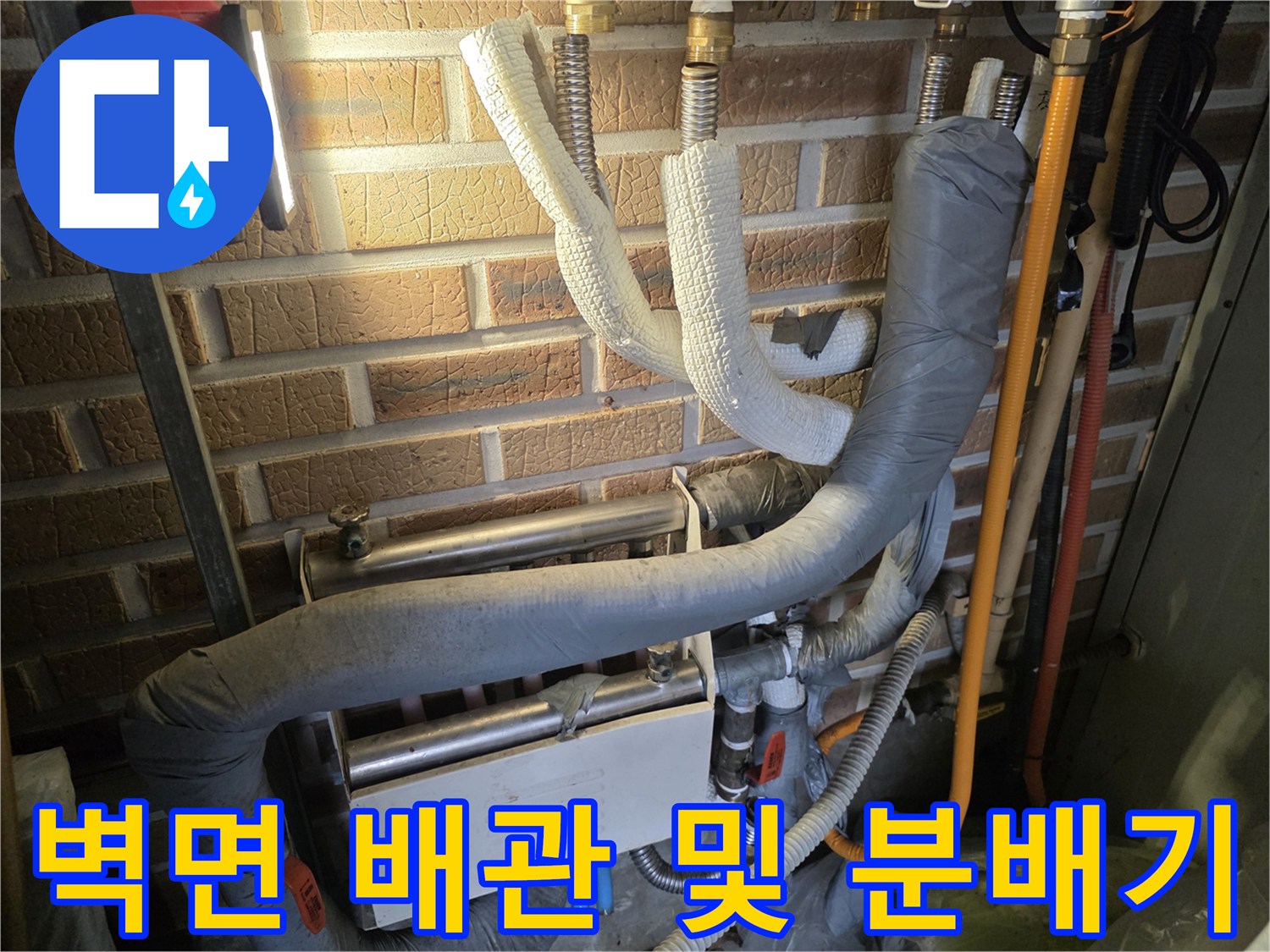 벽돌 벽면에 고정된 금속 배관과 보온재 처리된 호스들의 연결 상태
