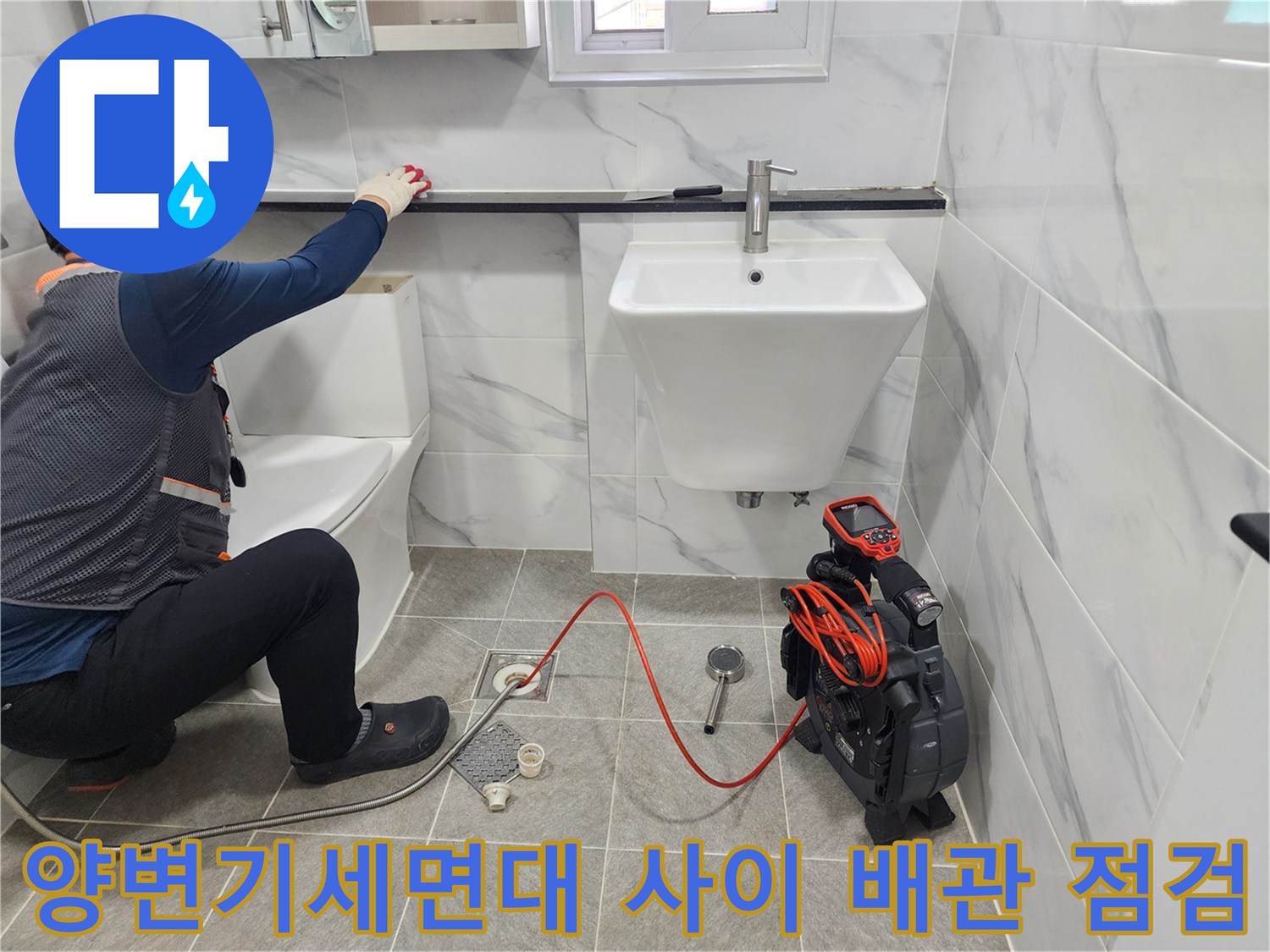 화장실 내 세면대와 양변기 사이의 공간에서 배수 시스템을 정밀하게 체크하는 장면