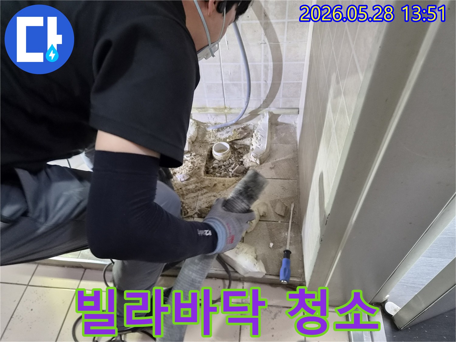 안전 장비를 착용한 기술자가-누수 배관 수리 후-바닥에 남은 잔해를-전문 청소기로 제거하고 있습니다.
