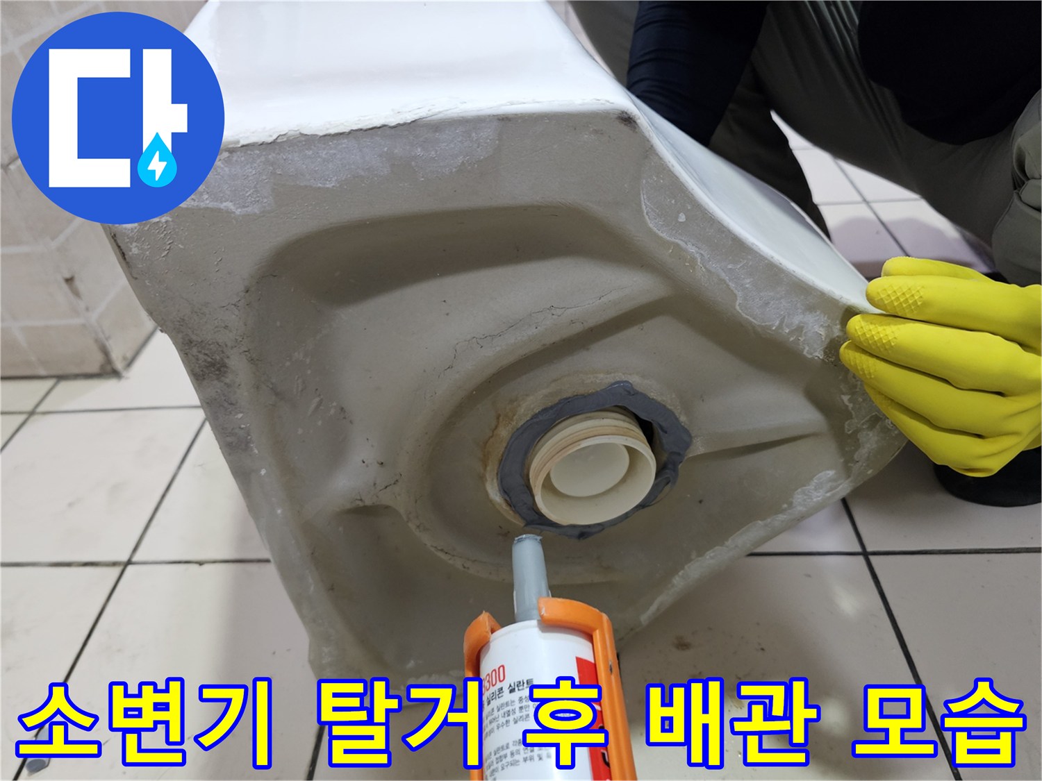 탈거된 소변기의 하부 배관과 작업용 실리콘 건의 근접 촬영