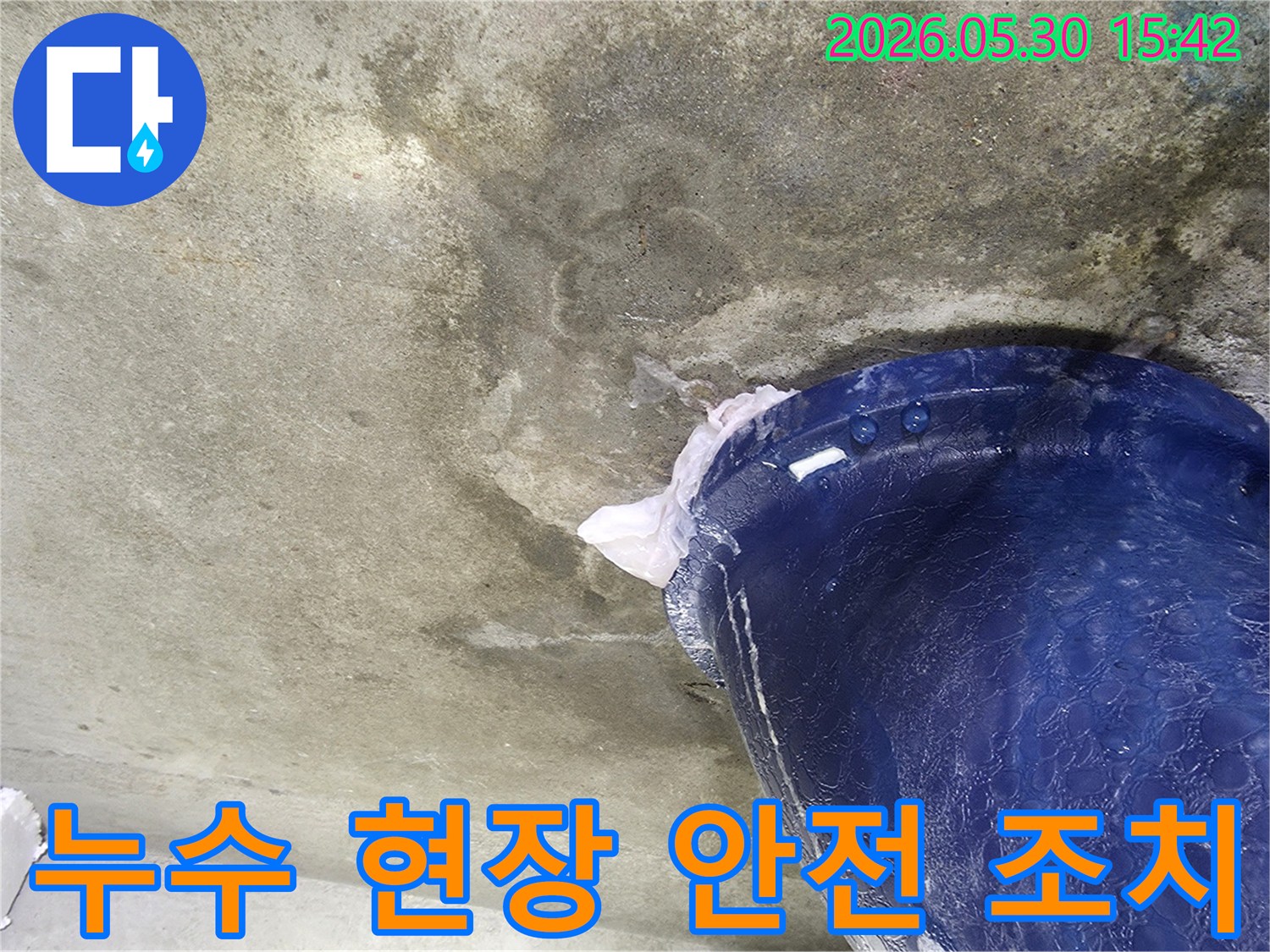 천장에서 물이 떨어지는 누수 현장에서-작업자의 안전과 추가 피해를 막기 위해-파란색 양동이로 물을 받아내는 안전 조치 모습입니다.