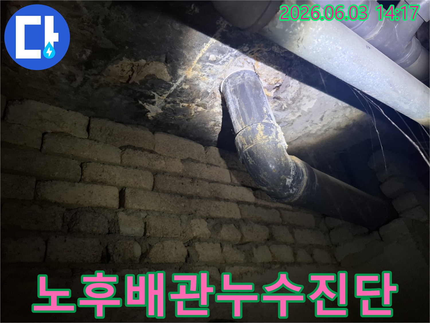 어두운 지하 공간의-낡은 벽돌 벽과-오래된 배관 주변에서-발견된 누수 흔적을-조명으로 비추어-정밀하게 진단하는 모습