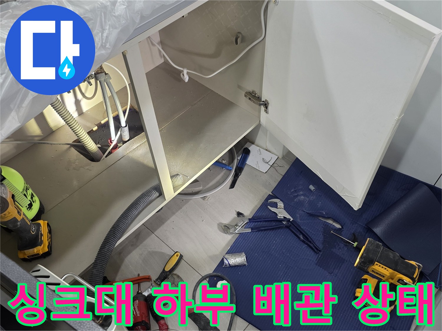 열려있는 싱크대 하부장 내부의 배관 구조와 바닥 작업 도구들