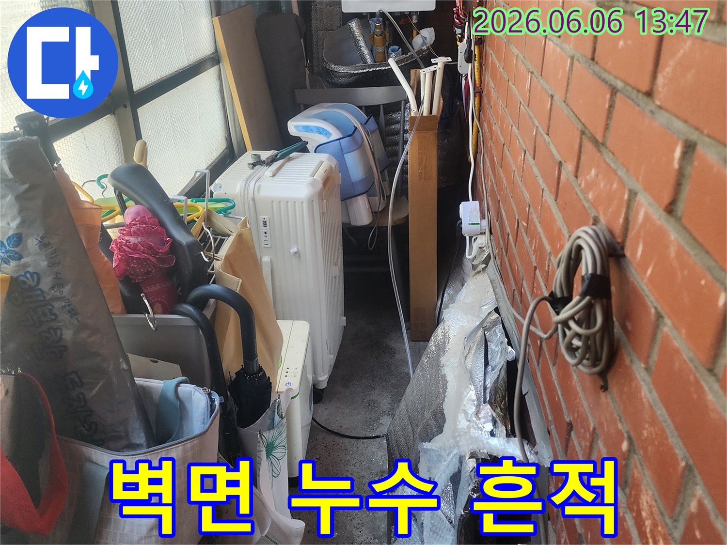 벽돌-벽-아래-복잡하게-얽힌-배관과-생활-용품들-사이에서-발견된-누수-흔적을-보여주는-사진