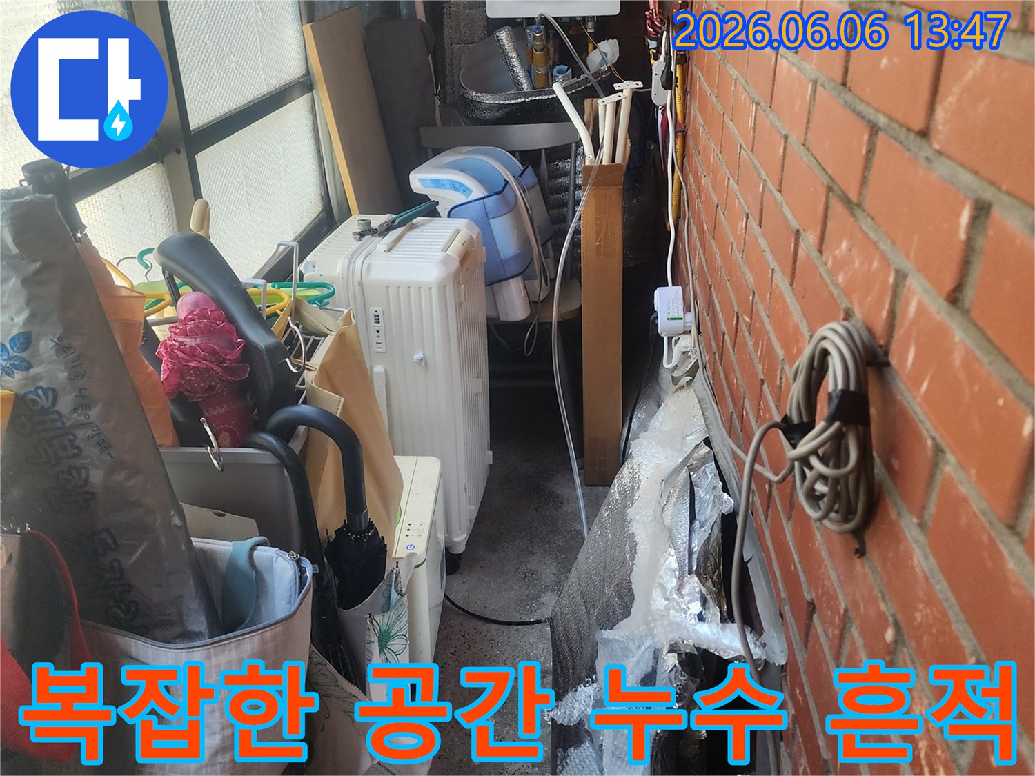 벽돌-벽-아래-복잡하게-얽힌-배관과-생활-용품들-사이에서-발견된-누수-흔적을-보여주는-사진