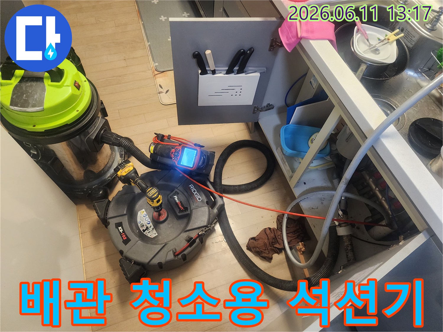 주방 싱크대 밑에서 배관 이물질을 제거하기 위해 가동 중인 전문 장비 세트입니다.