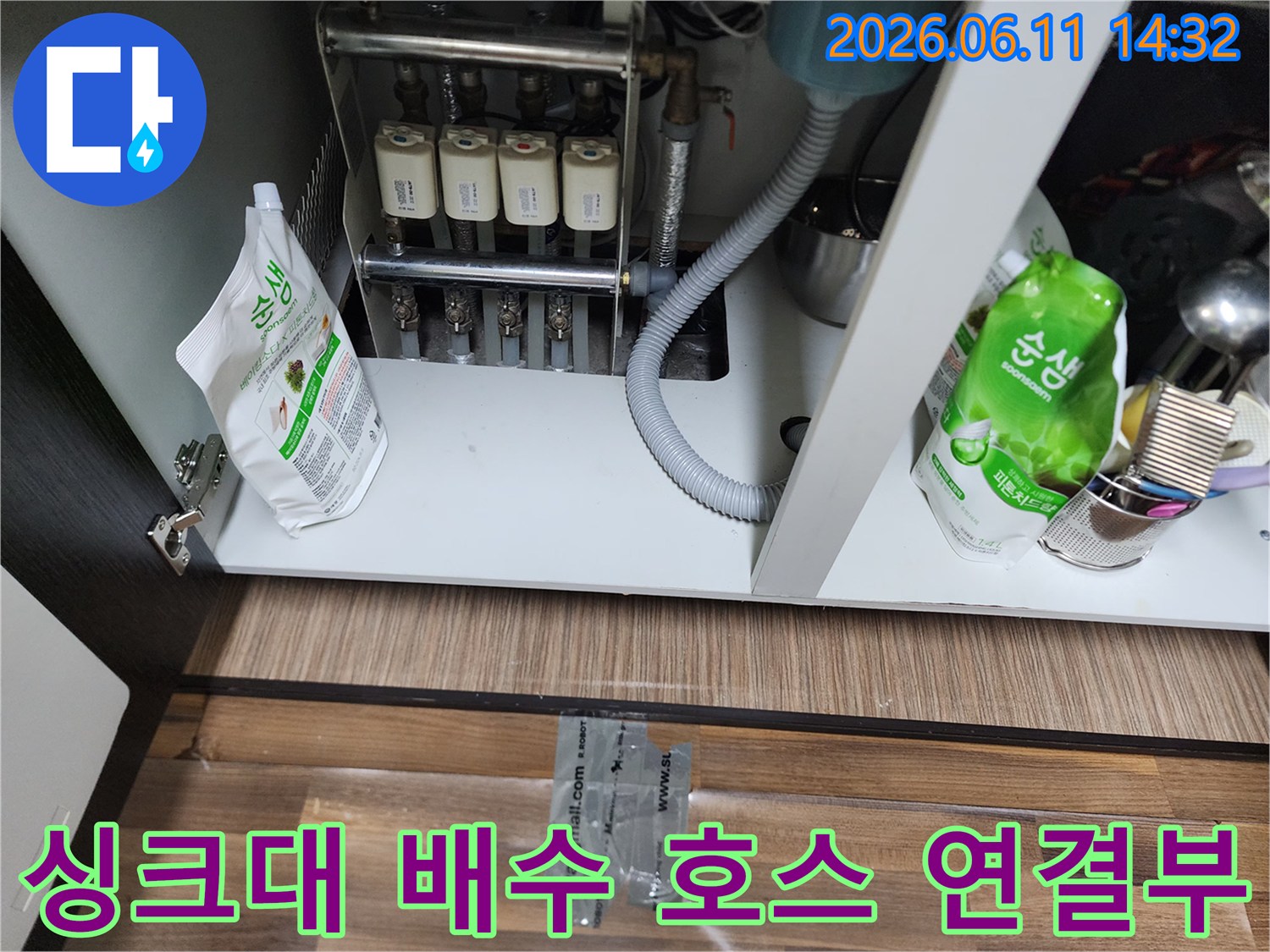 하얀색 정수 필터와 회색 주름 호스가 연결된 싱크대 아래쪽 모습입니다.