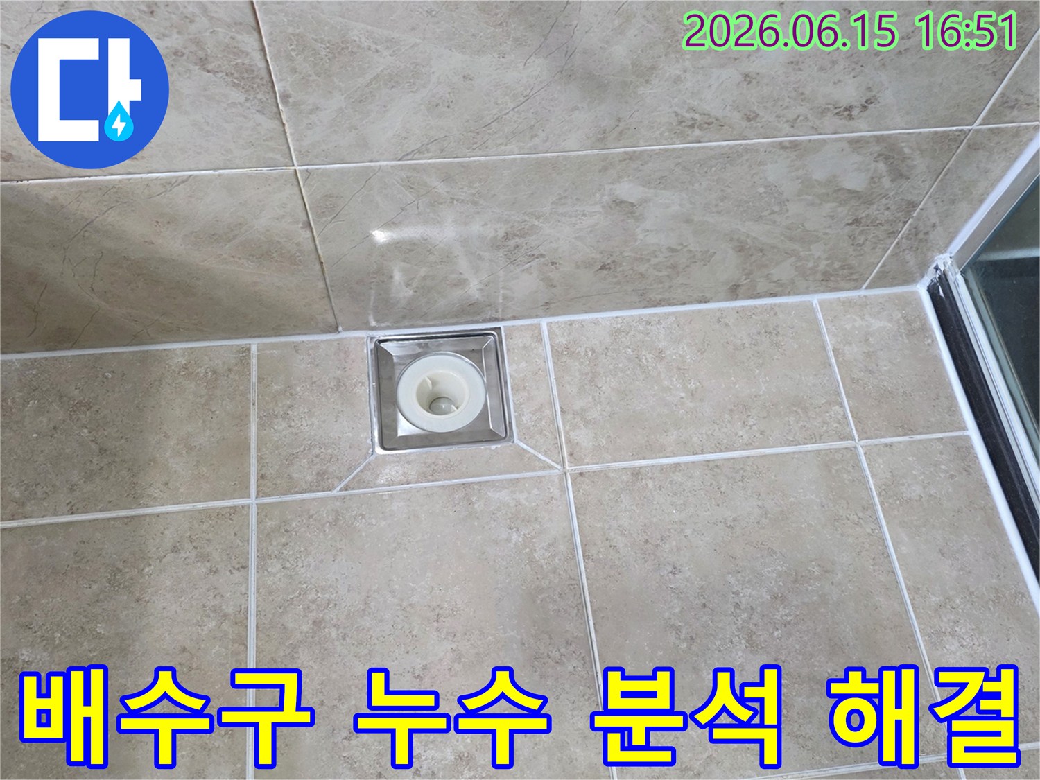 베이지색 타일 바닥에 설치된-사각형 금속 배수구의 모습으로-주변 타일과 줄눈의 상태를 면밀히 관찰하는 이미지입니다