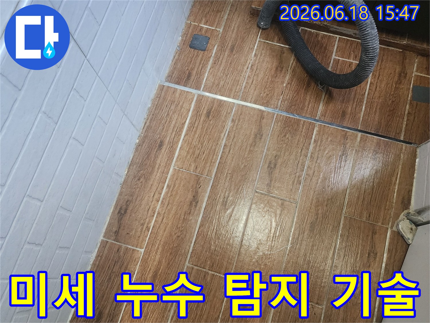 염창동 아파트에서 미세한 누수를 잡아내기 위한 정밀 탐지 작업이 진행 중인 현장 사진입니다-바닥 타일 위에 놓인 검은색 호스가 탐지 장비의 일부임을 보여줍니다.