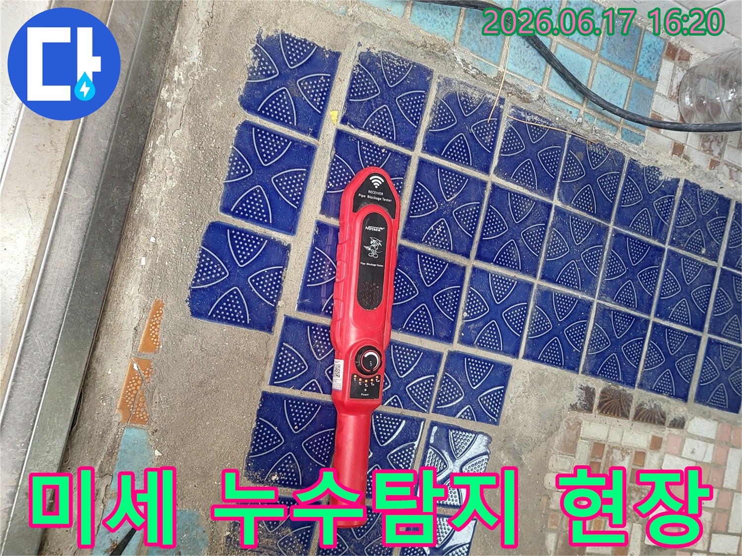 파란색 타일이 뜯겨나간 욕실 바닥에 놓인-붉은색 누수탐지 장비가-미세한 누수 지점을 찾는 중인 모습