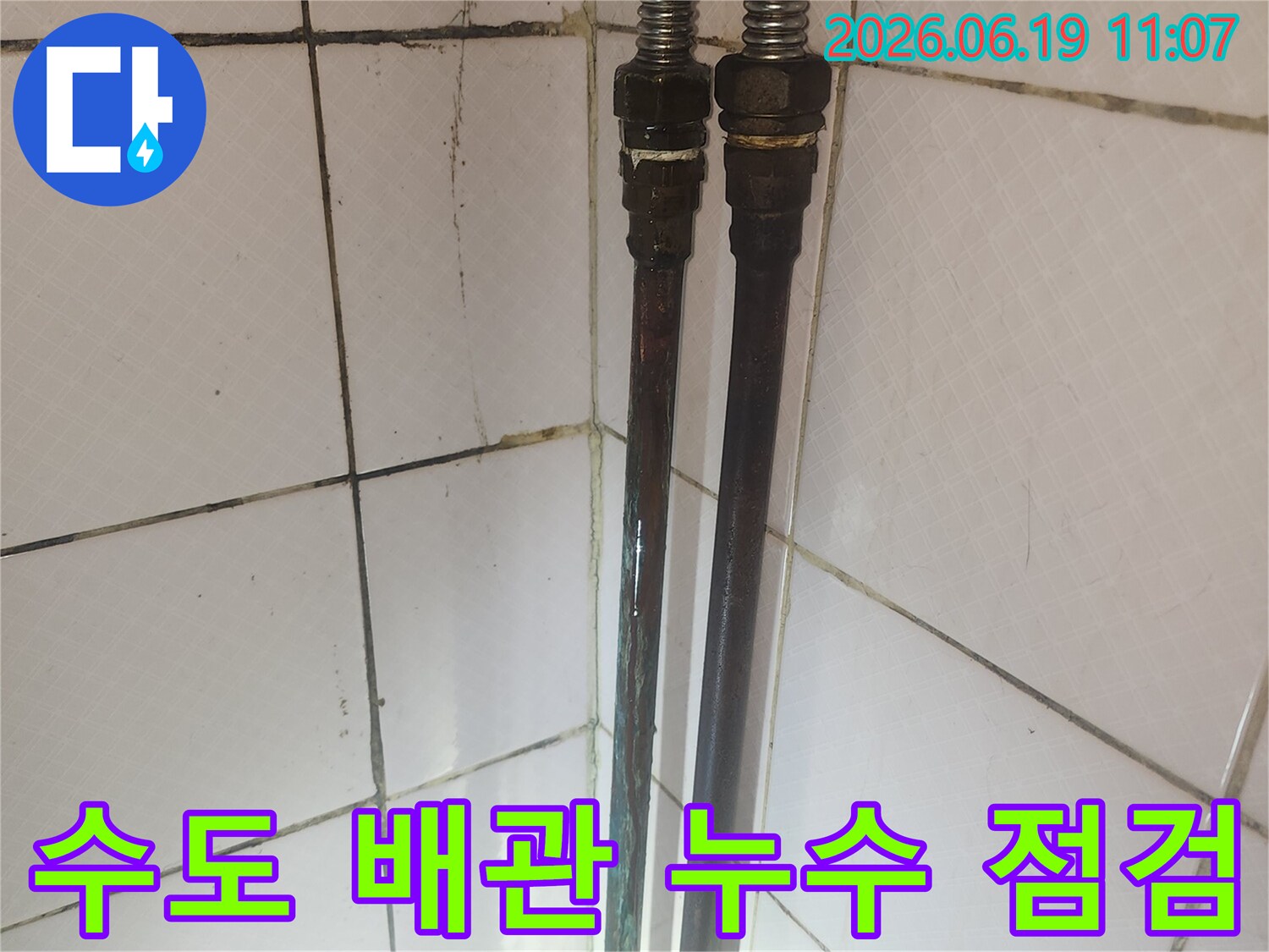 오래된 수도 배관의 연결 부위와 주변 타일의 상태를 보여주며-누수 점검 과정을 나타냅니다