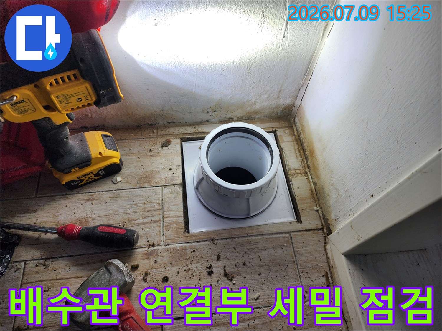 먼지 묻은 타일 위 배수 트랩과 공구들이 배치된 모습