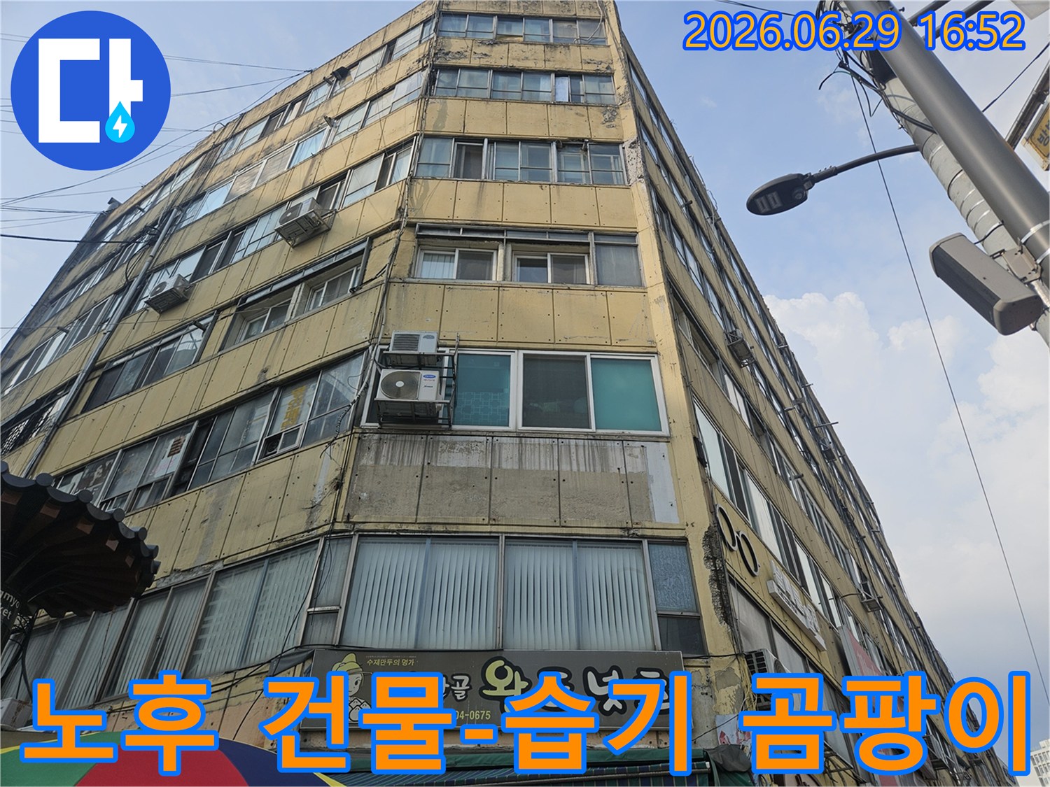 오래된 상가 건물의-외벽에 나타난-습기 흔적과-곰팡이 발생 가능성을-점검하는-전문가의-모습