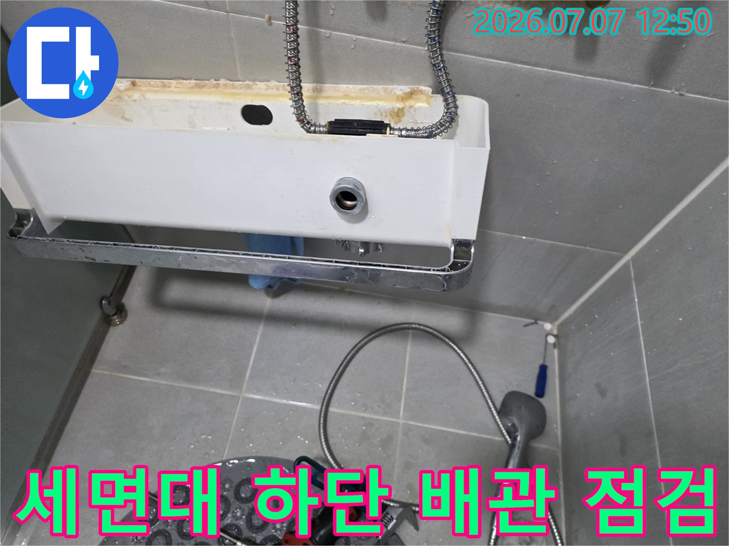 세면대 프레임 아래에 노출된 배관과 수도 호스 연결부를 정밀하게 진단하는 모습