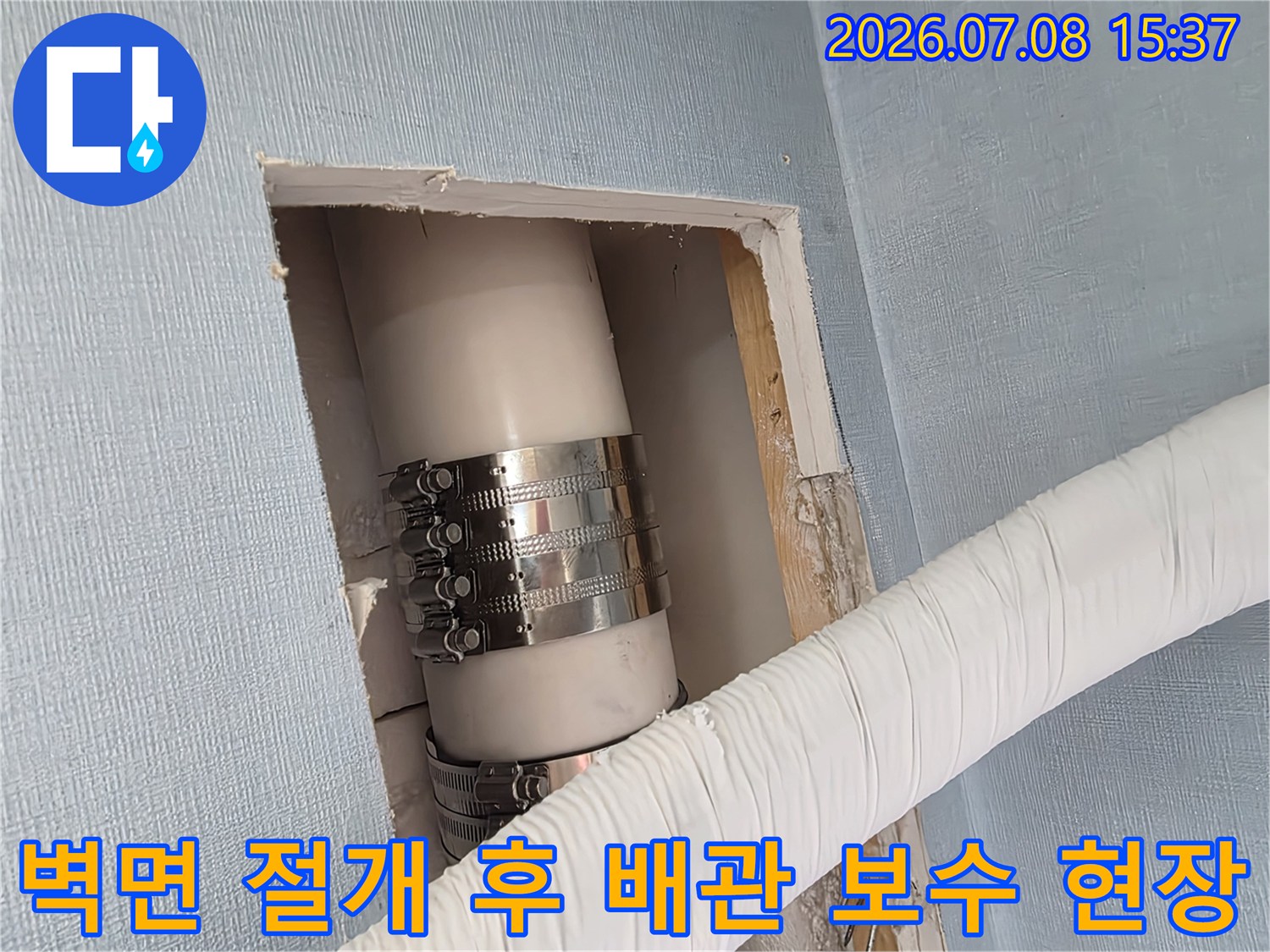 벽체를 절개하여 노출된 에어컨 배수관과 금속 밴드로 고정된 배관 연결부위