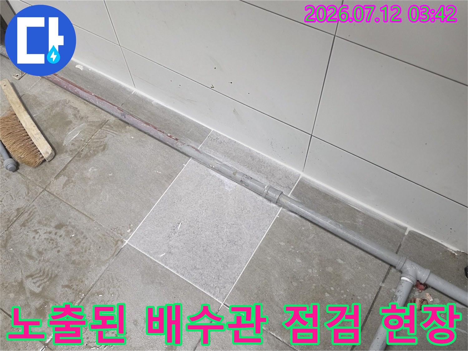 바닥 타일이 제거되고 노출된 회색 PVC 배수관과 작업용 브러시가 놓인 현장 모습