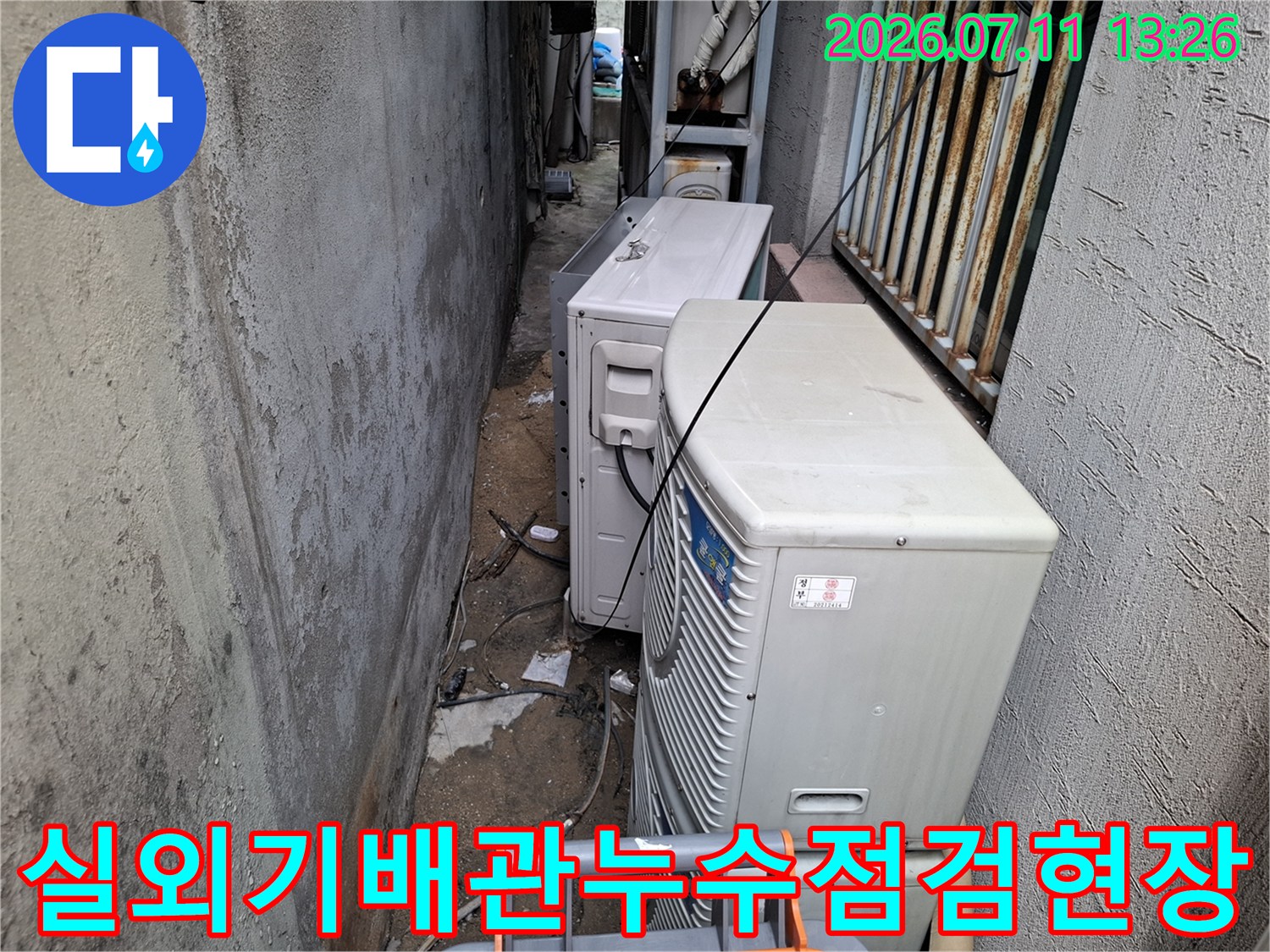실외기들이 배치된 좁은 공간에서 드레인 배관을 점검하는 모습