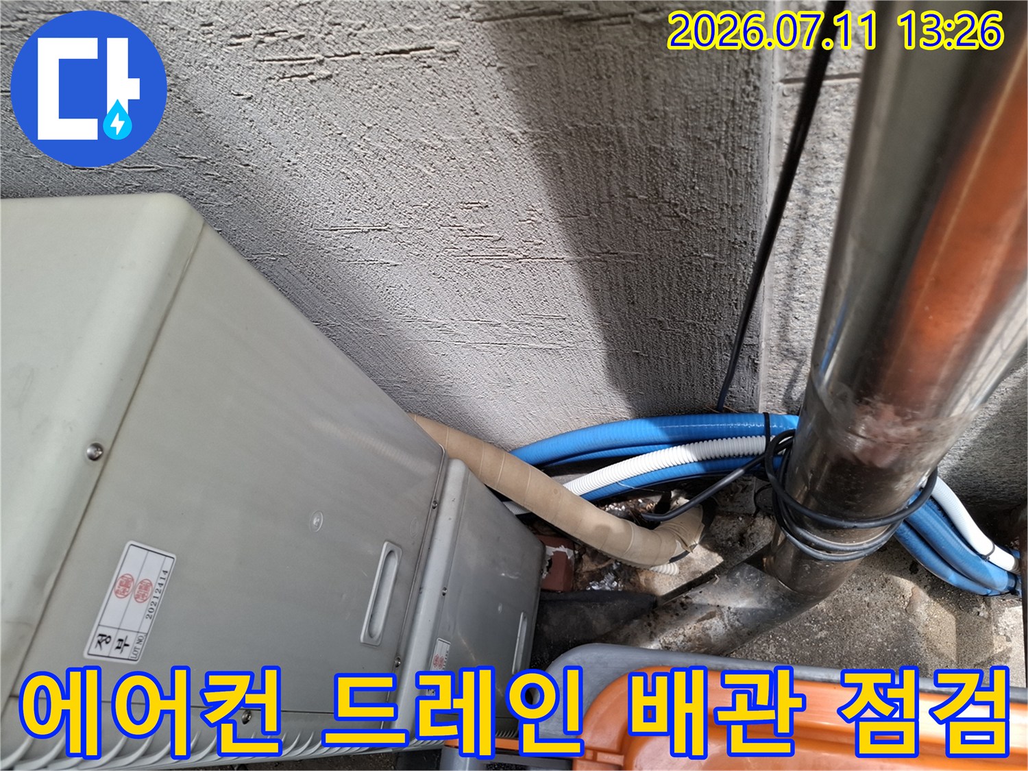 에어컨 실외기 옆으로 지나가는 파란색과 흰색의 드레인 배관 연결부위 점검 모습