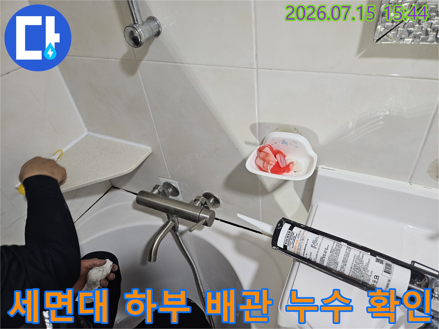 세면대 아래쪽의 수도 배관 연결 부위를 상세히 점검하고 있는 장면