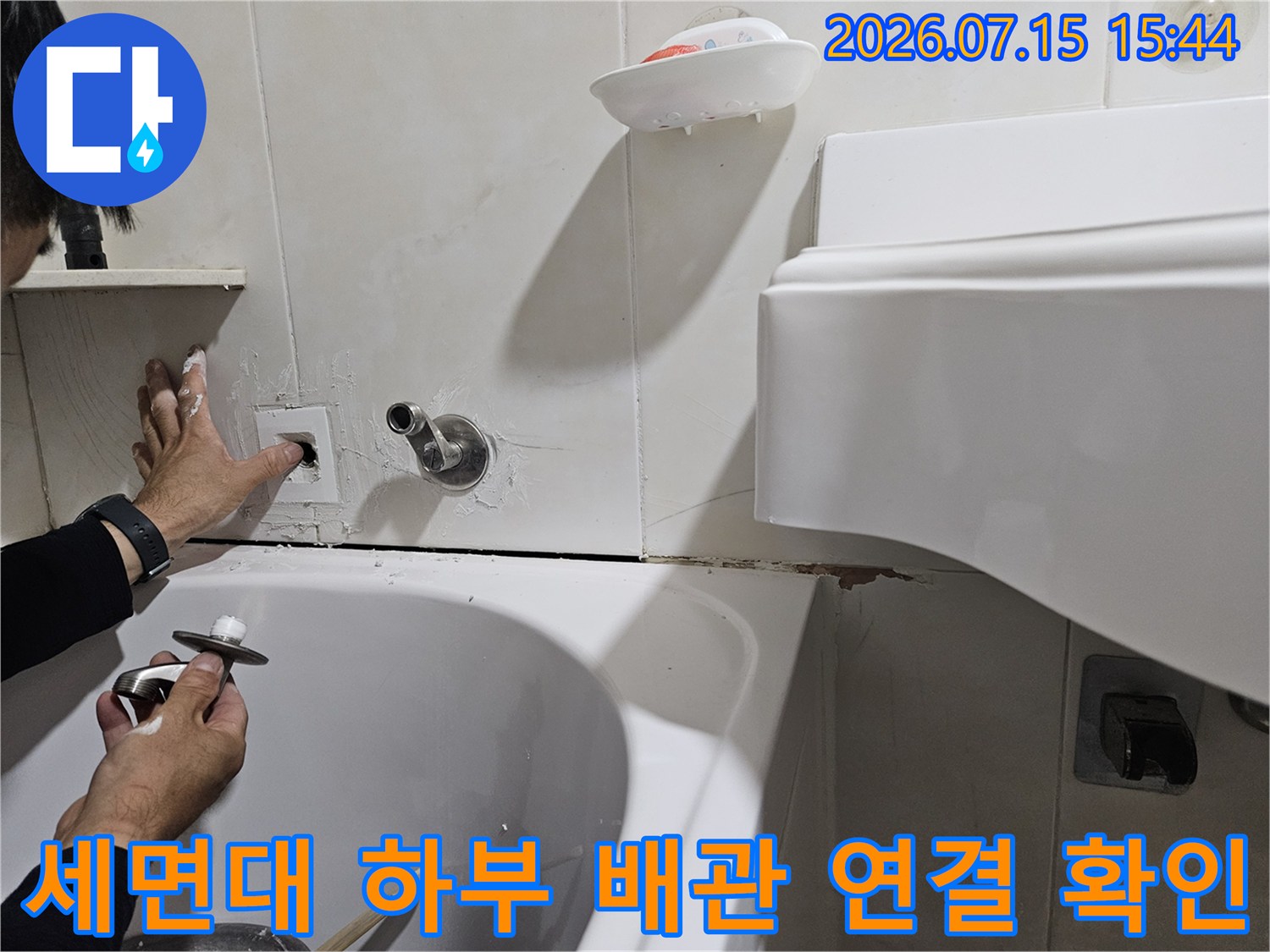 작업자가 세면대 아래 배관을 직접 손으로 잡아 점검하는 모습