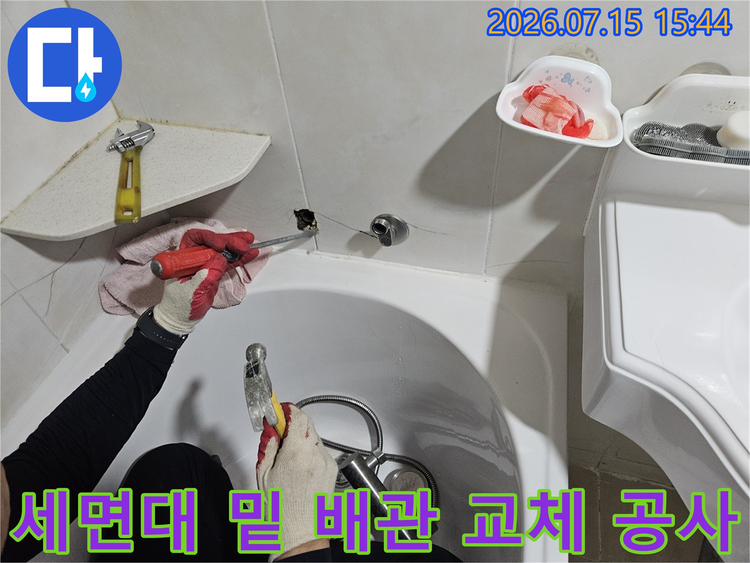장갑을 끼고 세면대 아래쪽 파손된 배관 부위를 수리하는 기술자의 손길
