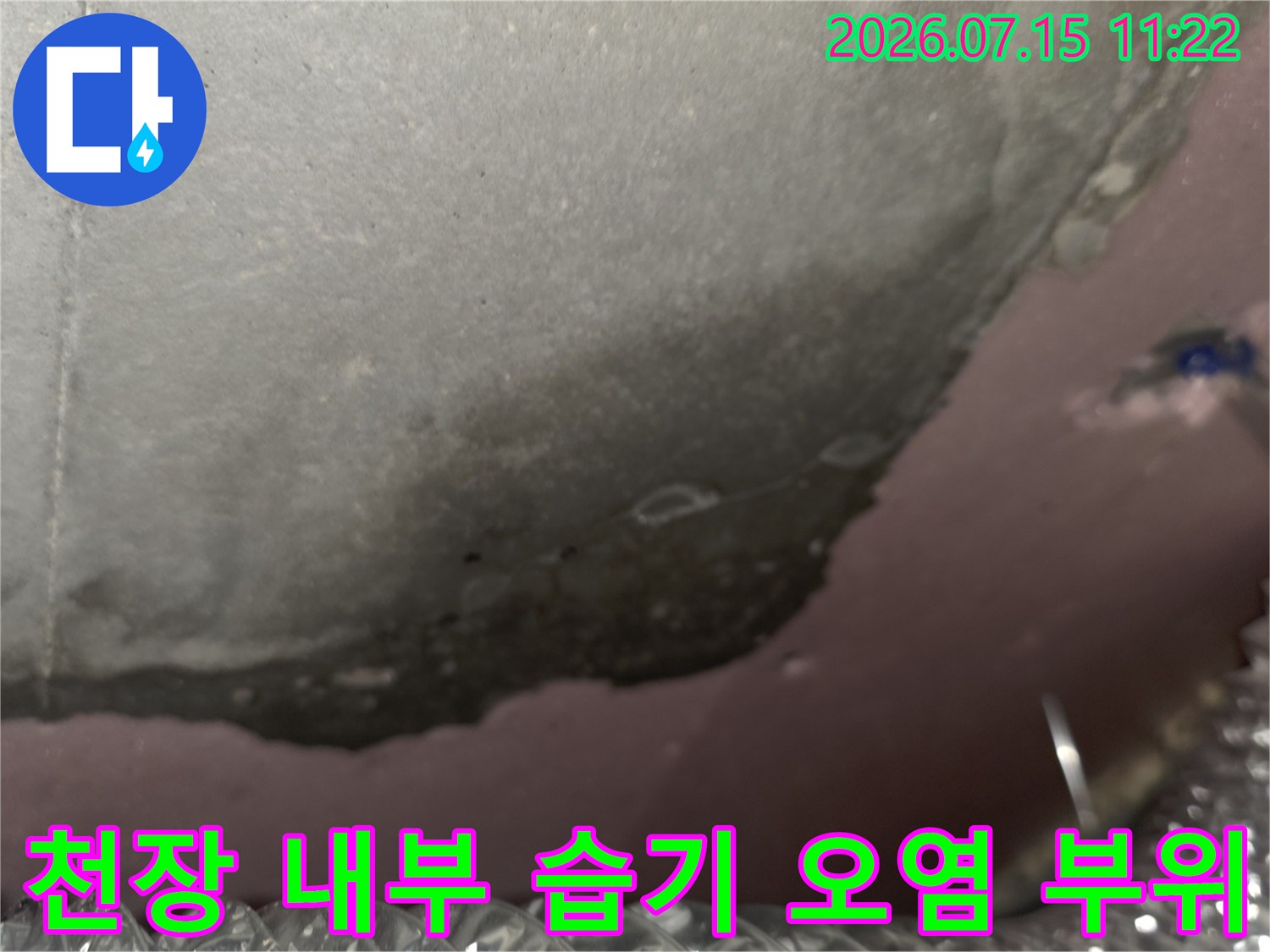 천장 내부에 형성된 어두운 색의 누수-오염 구역과 배관 연결부