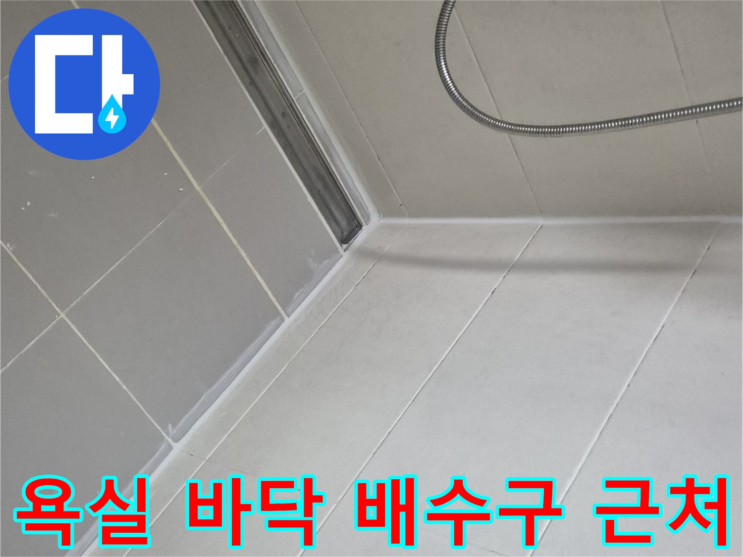 샤워기 호스와 연결된 화장실 바닥의 타일 및 배수구 사진입니다.