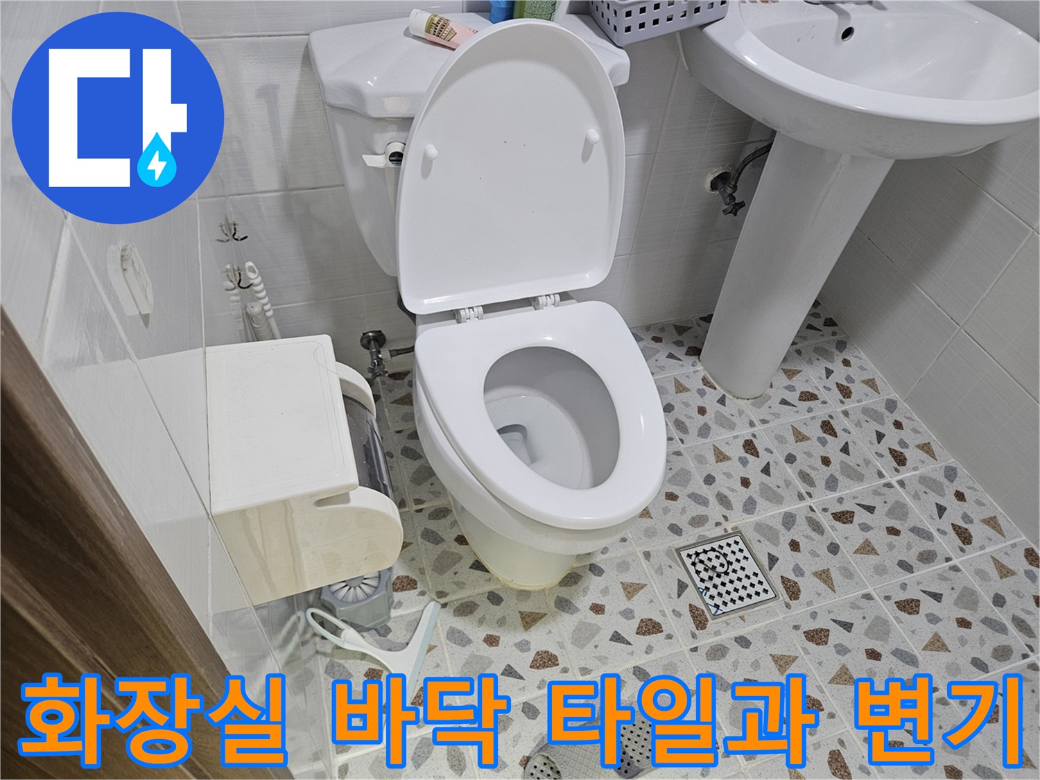 변기 옆 화장실 배수구와 모자이크 패턴의 타일 벽면 사진입니다.