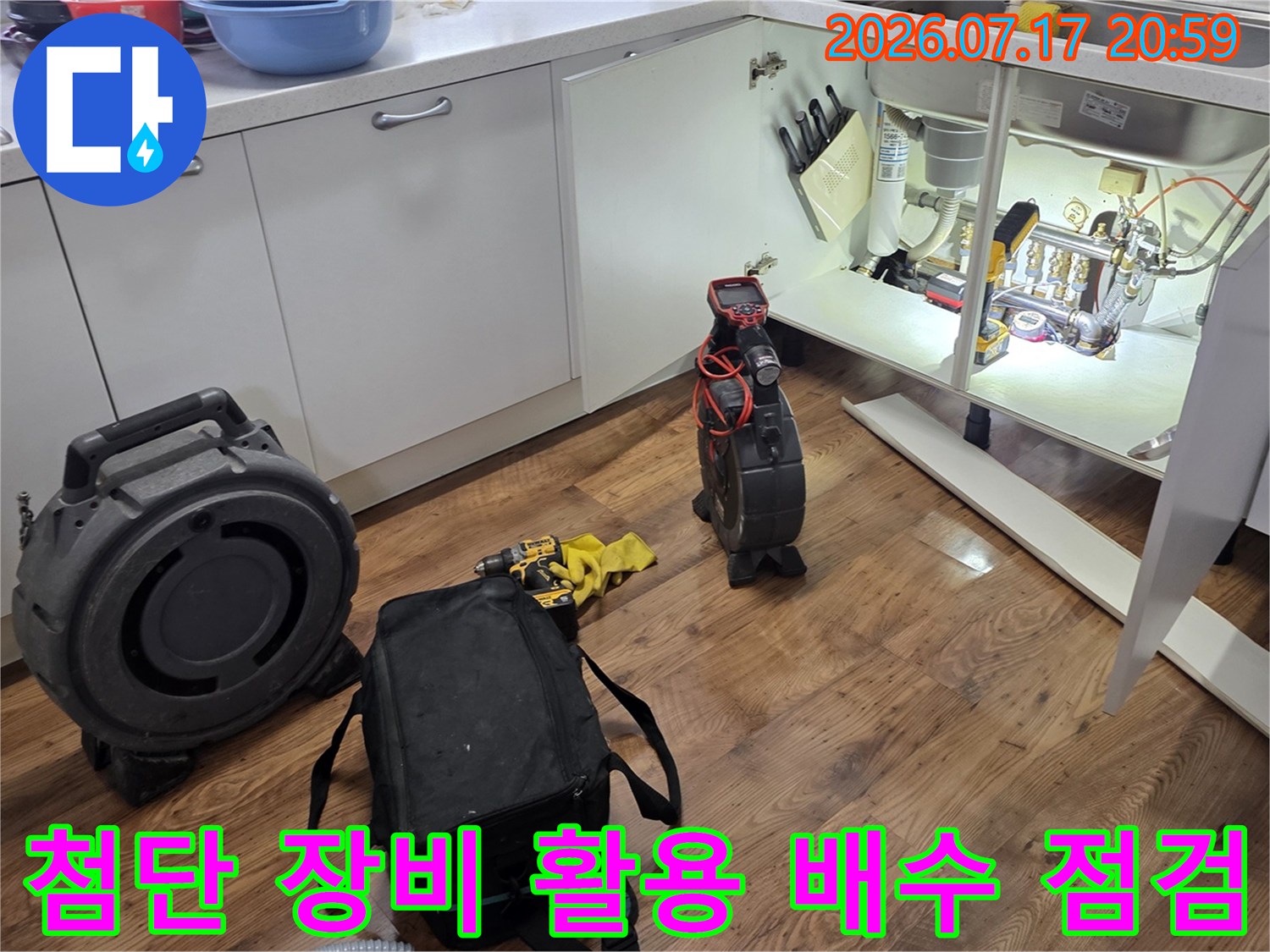 싱크대 밑 공간에서 전문가 전용 가방과 탐지기로 하부 배수 시스템을 면밀히 진찰하는 모습