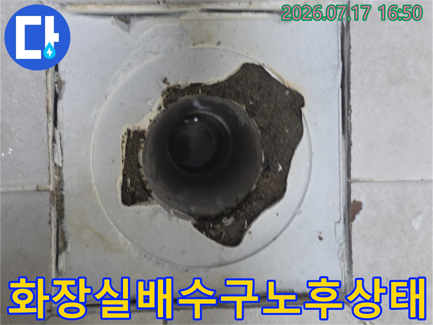 마모된 화장실 배수구 주변의 파손된 마감재와 노출된 배관 부위