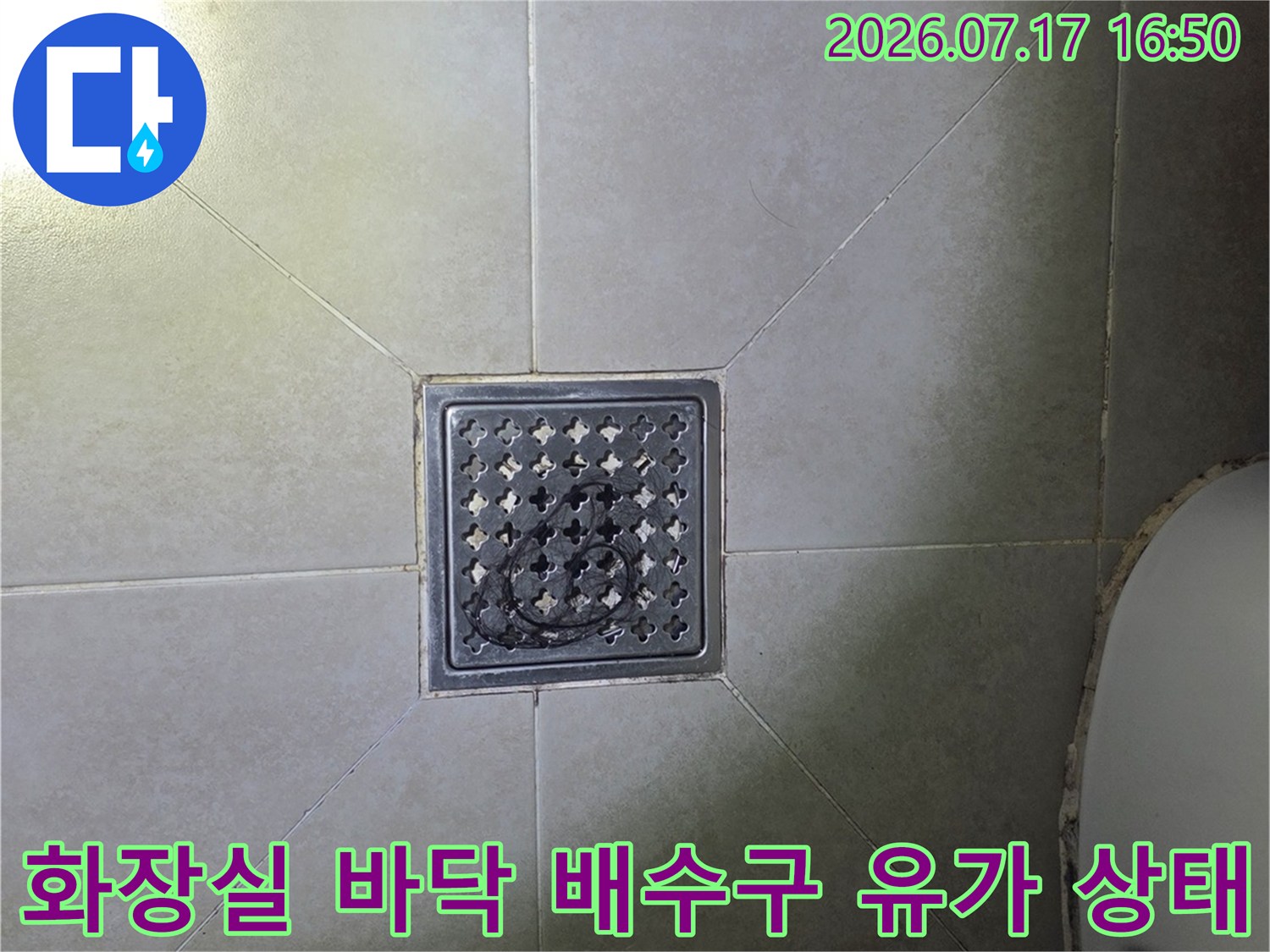 화장실 바닥 타일 중앙에 설치된 스테인리스 재질의 사각 배수구-유가 모습