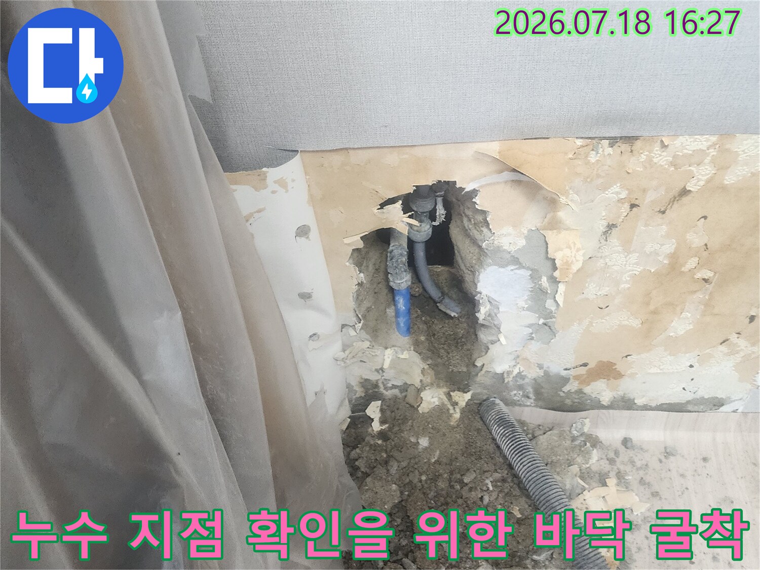 바닥재를 제거하고 파헤친 공간 속에 파란색 수도 배관이 드러나 있는 모습
