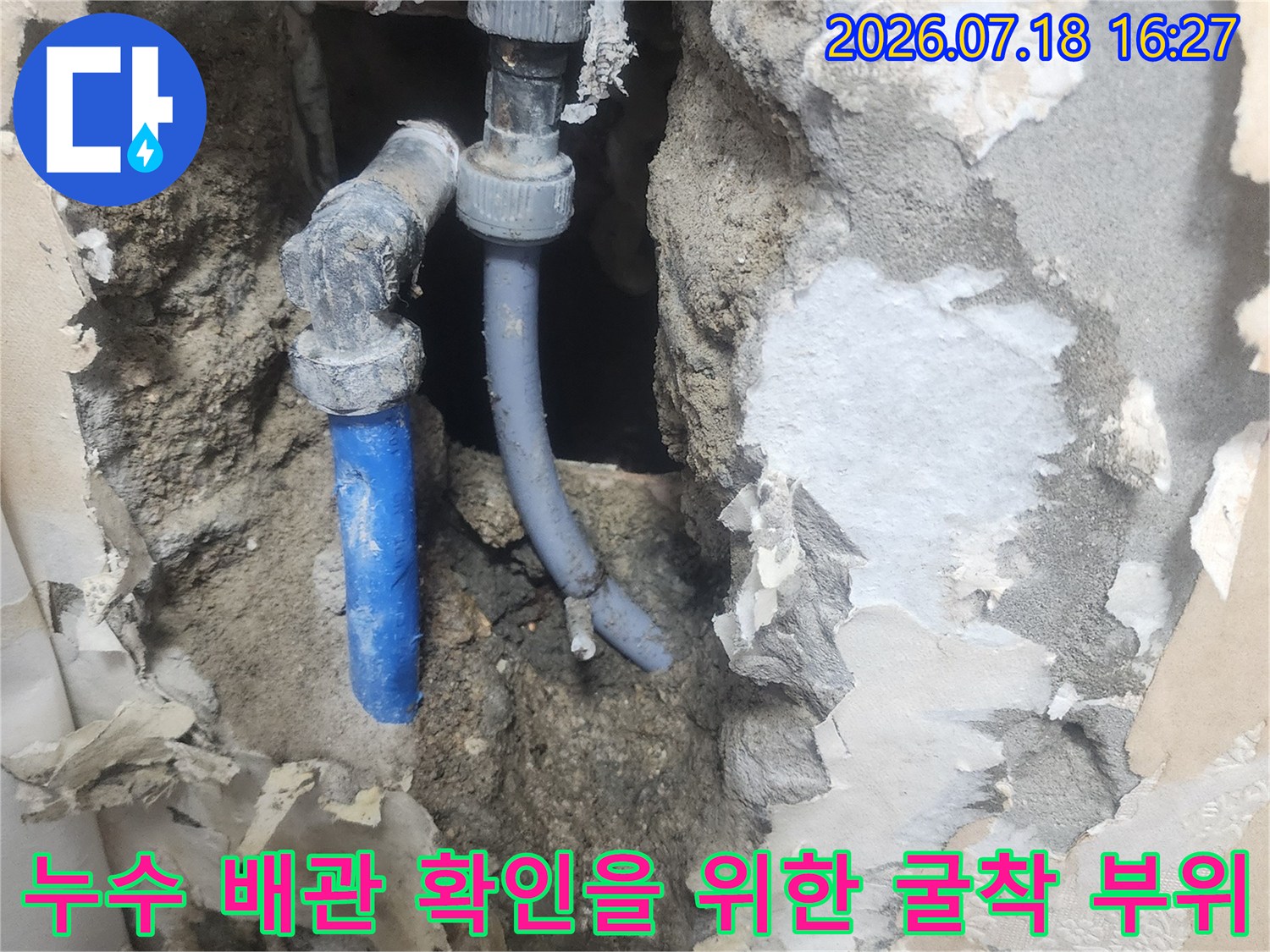 회색 콘크리트 가루와 함께 노출된 파란색 수도 배관의 모습
