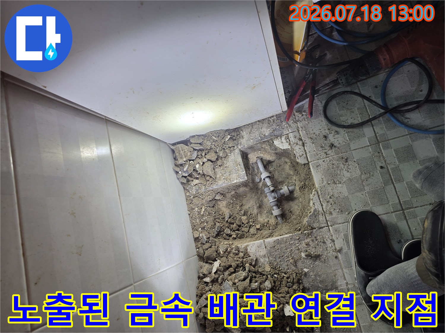 타일과 시멘트 층을 제거하여 드러난 은색 금속 수도 배관-연결 소켓 부분
