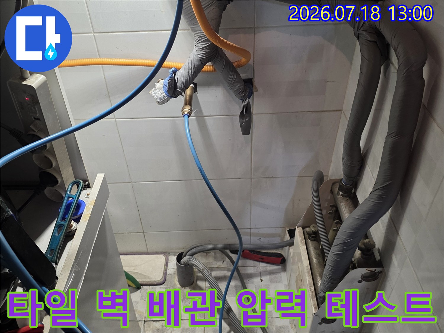 흰색 타일 벽에 설치된 여러 가닥의 보온재 배관과 연결된 파란색 탐지선-누수 검사 중