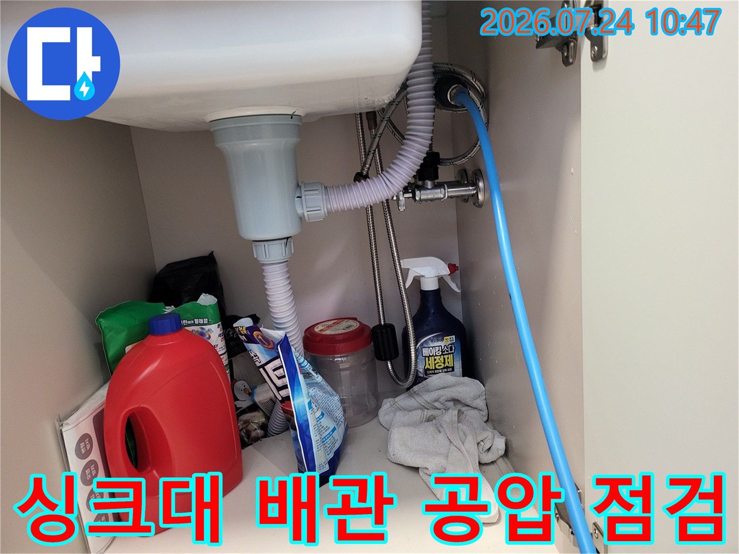 싱크대 아래에 연결된 회색 배수관과 파란색 압력 테스트 호스가 연결된 장면