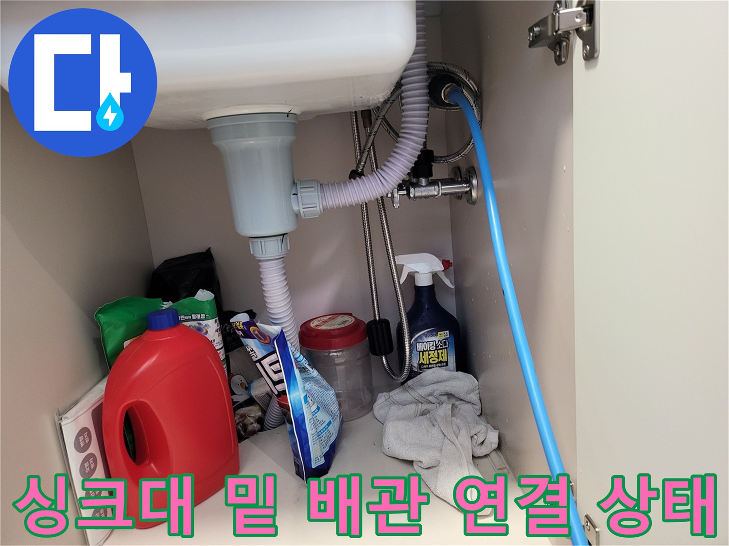 주방 싱크대 하단의 배수 호스와 점검용 파란색 호스 구성