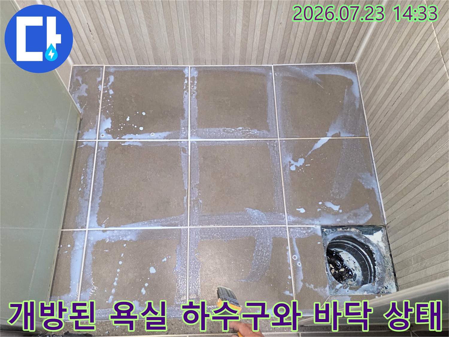 오른쪽-하단에-배수구가-개방되어-있고-타일에-흰색-얼룩이-있는-욕실-전경